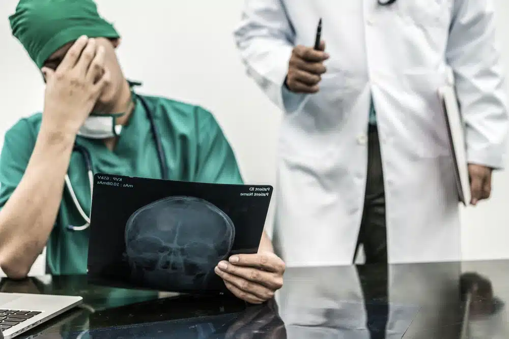 Surgical doctor covering his face with hand (face palm) expressing disappointment while holding x-ray film on office desk.