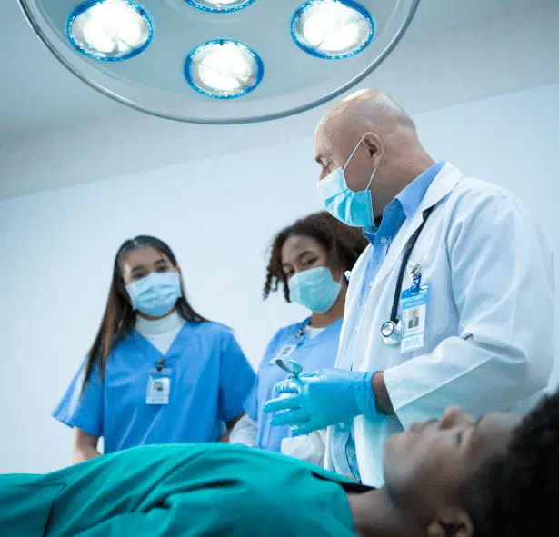 Doctor and nurses are gathered around a hospital bed, engaged in a focused discussion as the patient listens or rests.