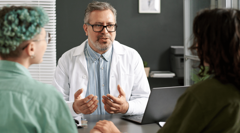 Image shows a doctor is explaining something to two patients sitting in front of him.