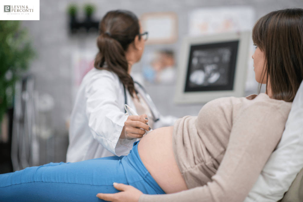 A pregnant woman lies on an examination table, watching the ultrasound monitor as the technician gently moves the probe over her belly.