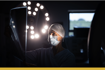 Doctor or nurse reviewing an x-ray in a dark room, there are lights behind her